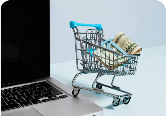 A shopping cart with money next to a laptop illustrating modern e-commerce and retail sectors.